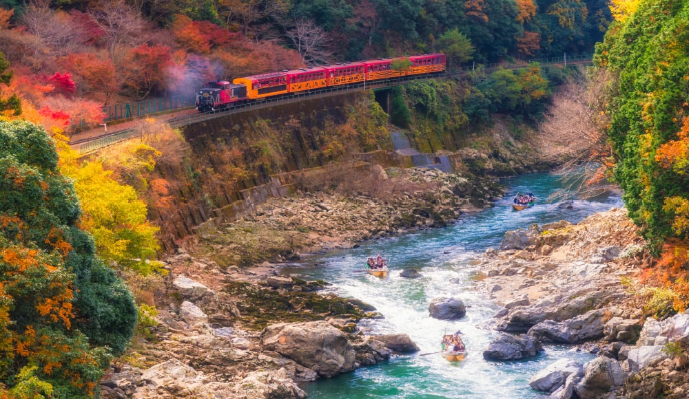 背景に紅葉とトロッコ列車が走る、保津川下りの様子